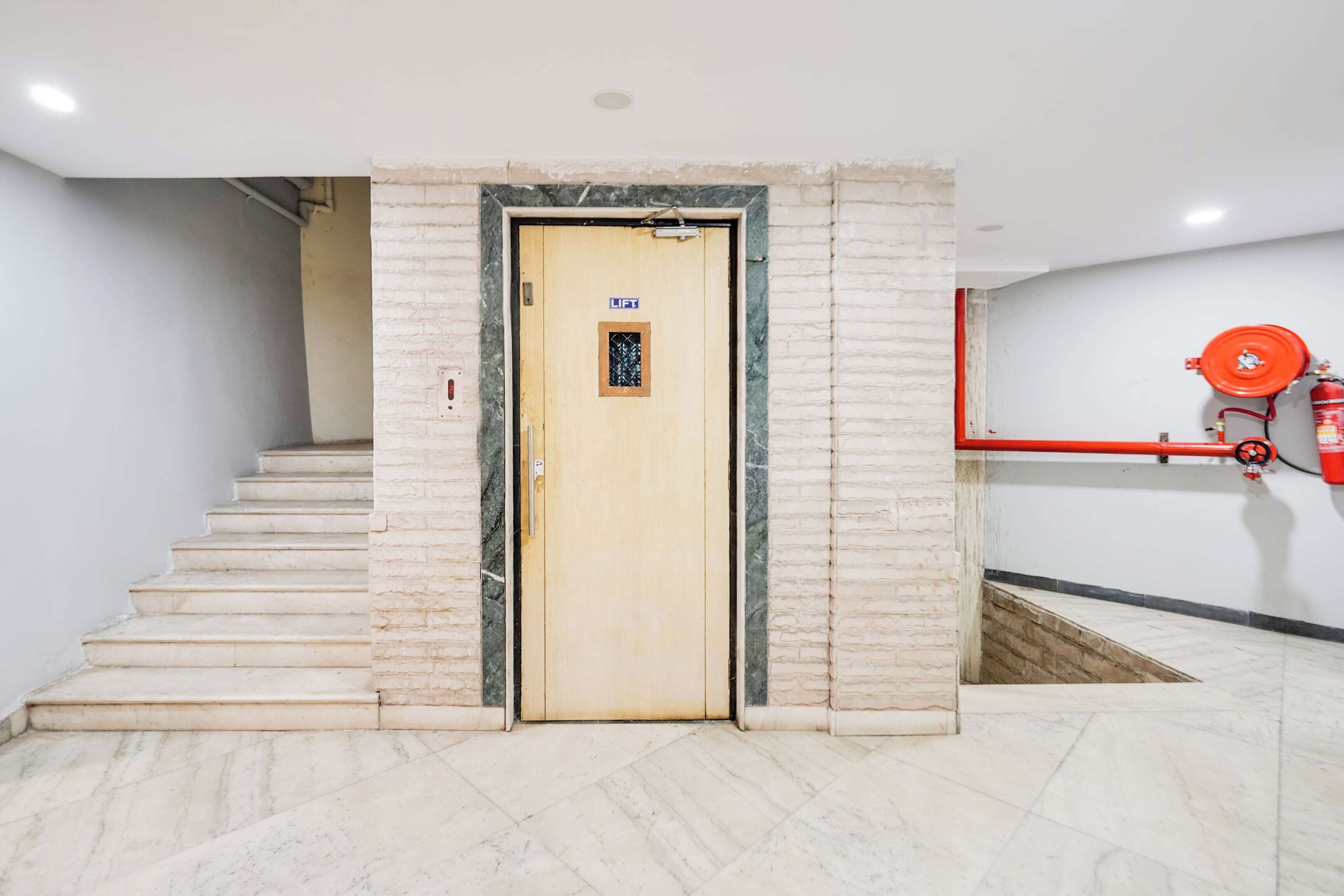 Entrada de hotel con una escalera de mármol que conduce a una puerta de ascensor con el rótulo 'LIFT'.