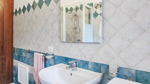 Un baño con lavamanos blanco, un espejo y una cabina de ducha.
