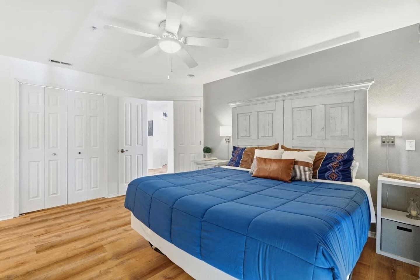 Une chambre à coucher avec un lit, un ventilateur de plafond, des murs blancs et un plancher en bois.