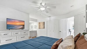 A bedroom with a large bed, a ceiling fan, a TV, a bathroom, and a door leading to another room. - Lakefront walk-in condo overlooking Marina (Branson)
