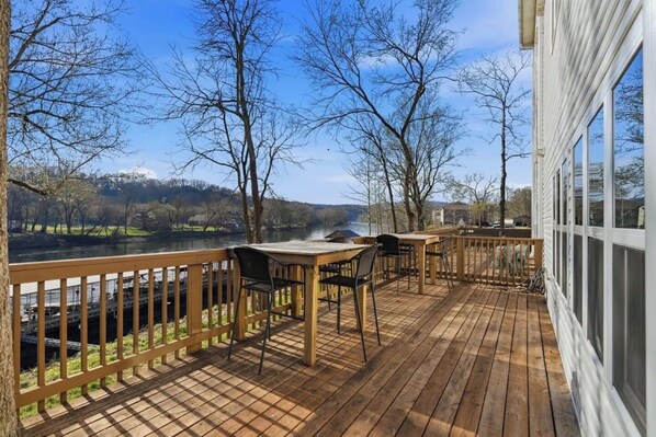 Un terrazzo in legno con tavolo e sedie, affacciato su un fiume e alberi.