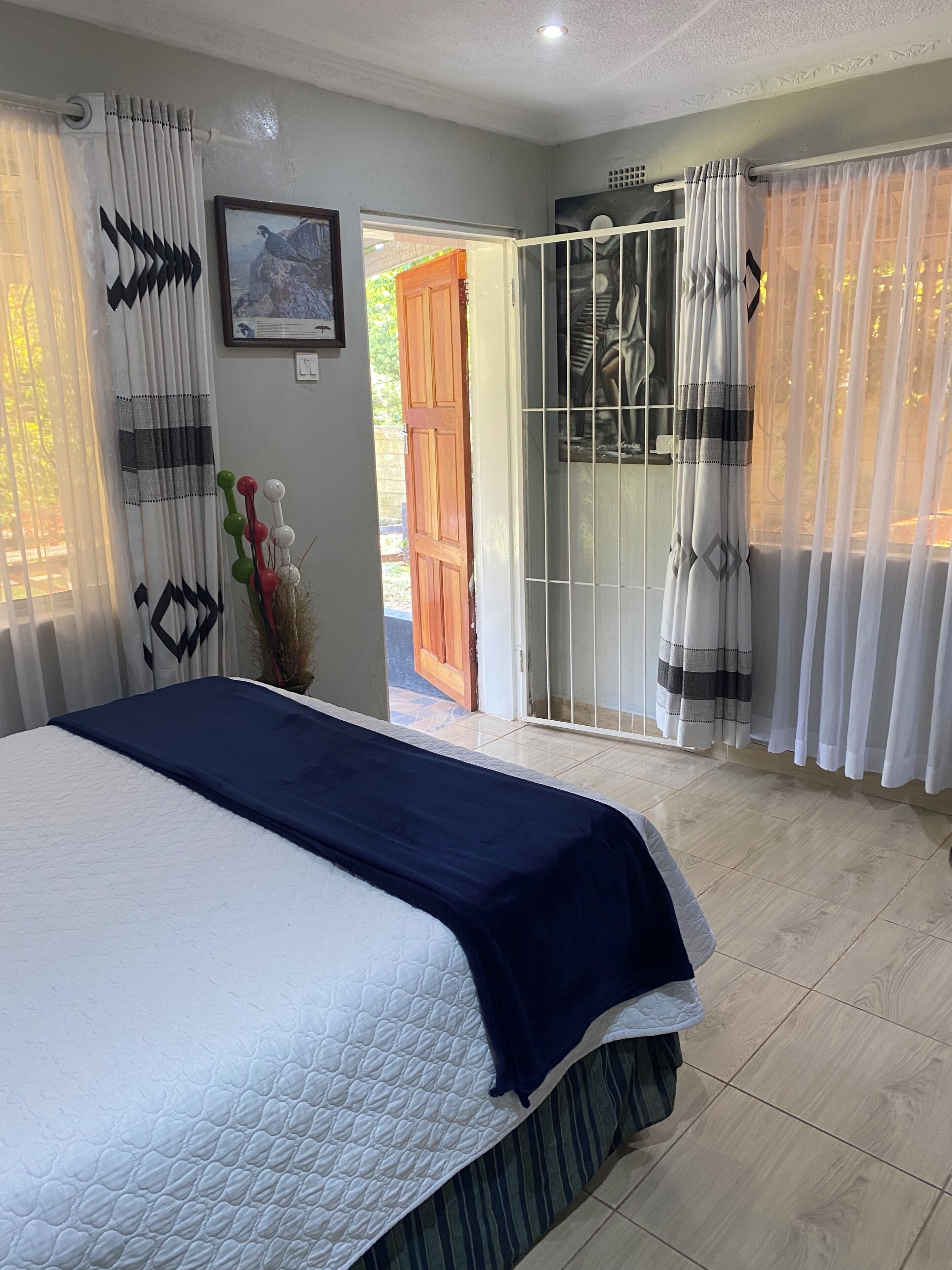 A bedroom with a bed, curtains, a door, and a view of the outside.