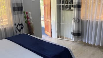 A bedroom with a bed, curtains, a door, and a view of the outside.