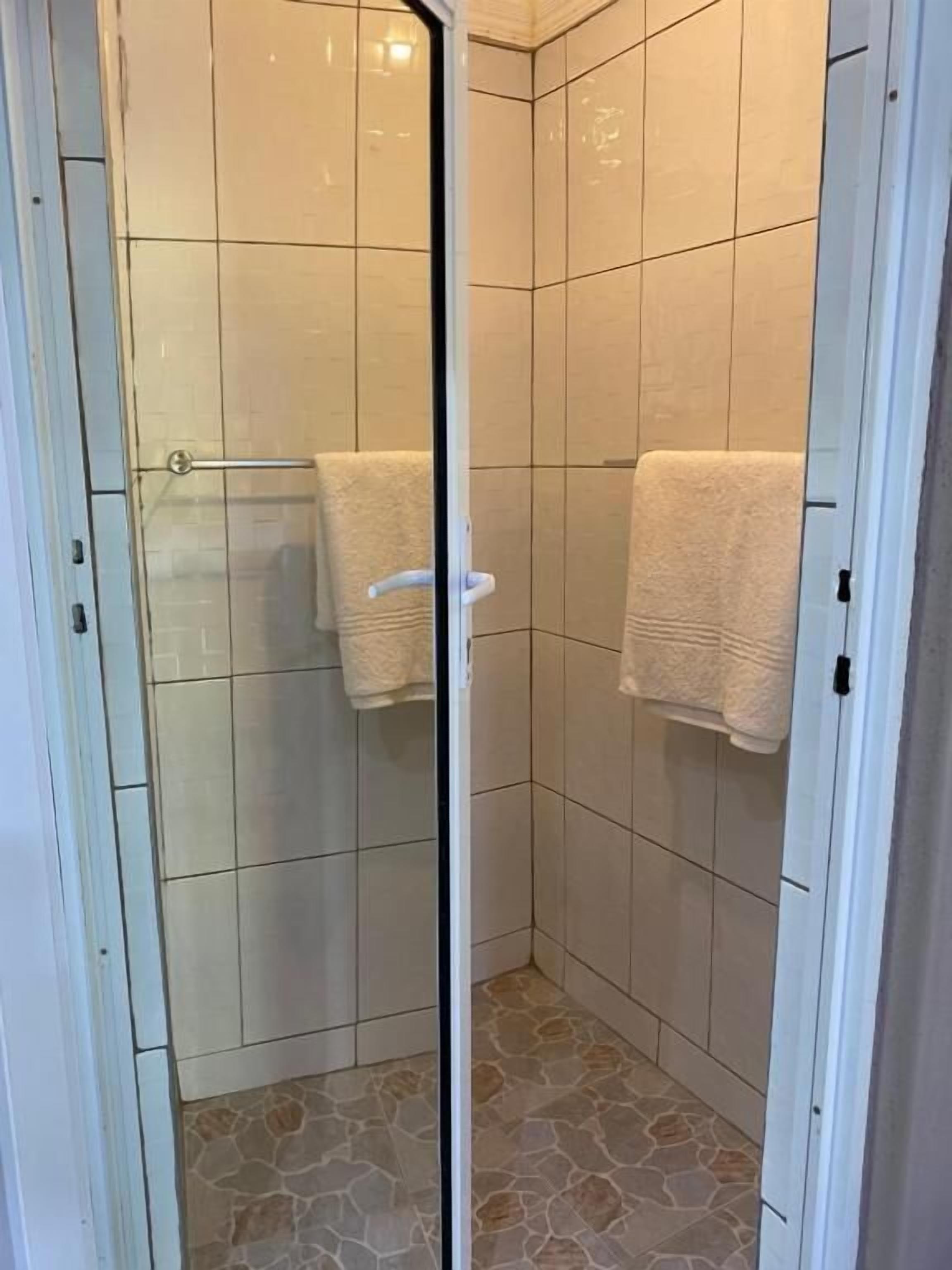 Ducha con puertas de cristal, paredes de azulejos y suelo de piedra.