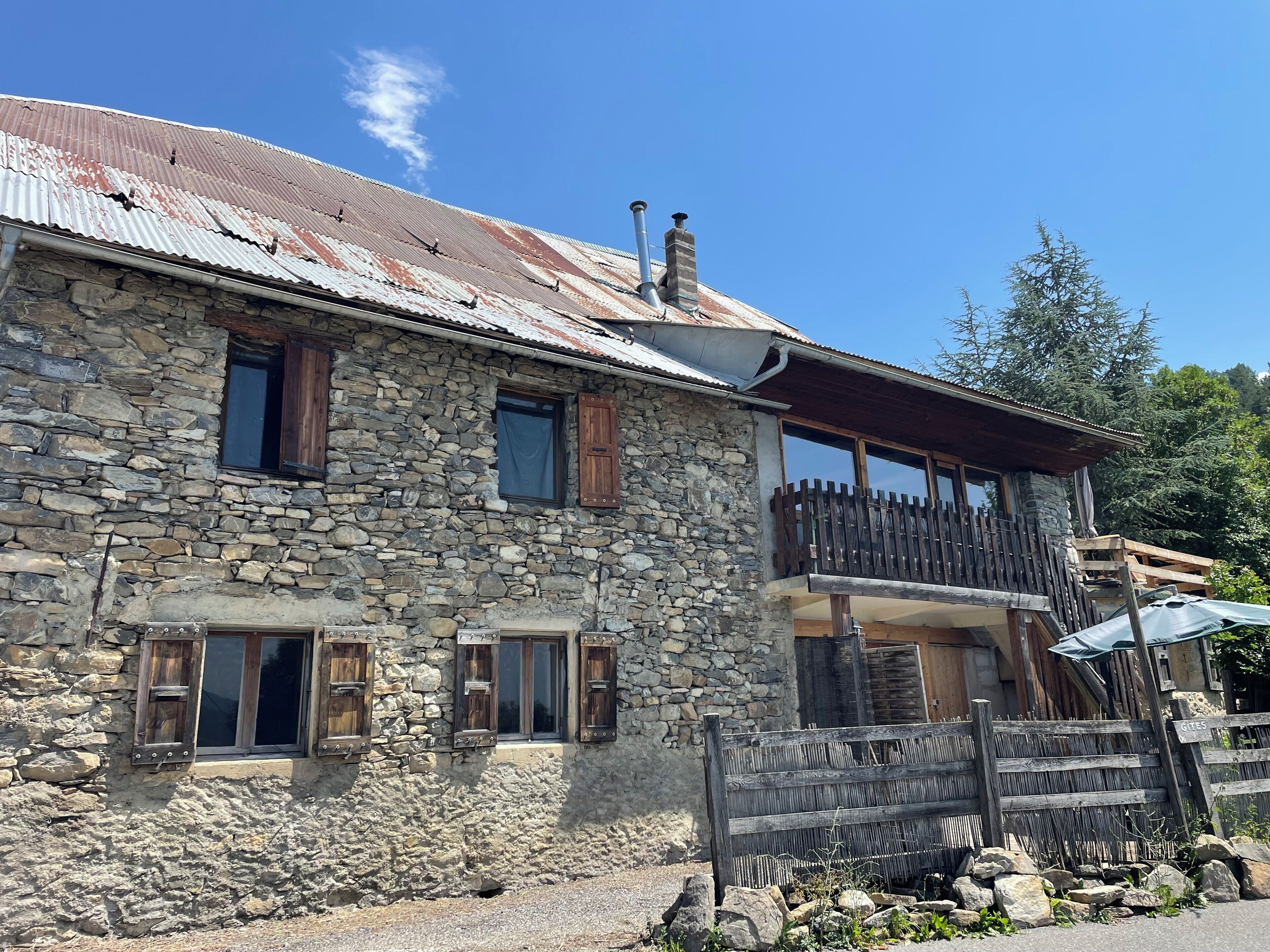 Ein Steinhaus mit einem hölzernen Balkon, einem Metall-Dach und einem Steinkamin.