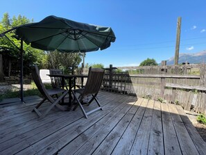 A wooden deck with a table and chairs under a green umbrella, surrounded by a wooden fence and greenery. - Lovely 2-bedroom apartment in enchanting Saint-Sauveur awaits you (Saint-Sauveur)
