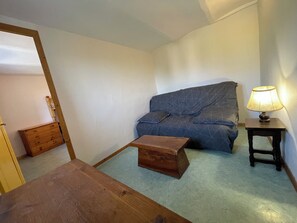 Ein kleiner Raum mit einer Schlafcouch, einem Holztisch, einer Lampe und einem Holzschrank.