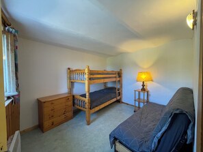 Ein Schlafraum mit Etagenbetten, einem Holzschrank, einem Nachttisch mit Lampe und einem Fenster mit Vorhängen.