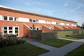 A multi-story brick building with a flat roof, a covered outdoor seating area, and a paved walkway. - Bork Harbor: Ringkobing Fjord (Hemmet)
