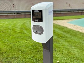 Un parquímetro electrónico blanco con pantalla y dos botones, situado al aire libre en una zona cubierta de césped.