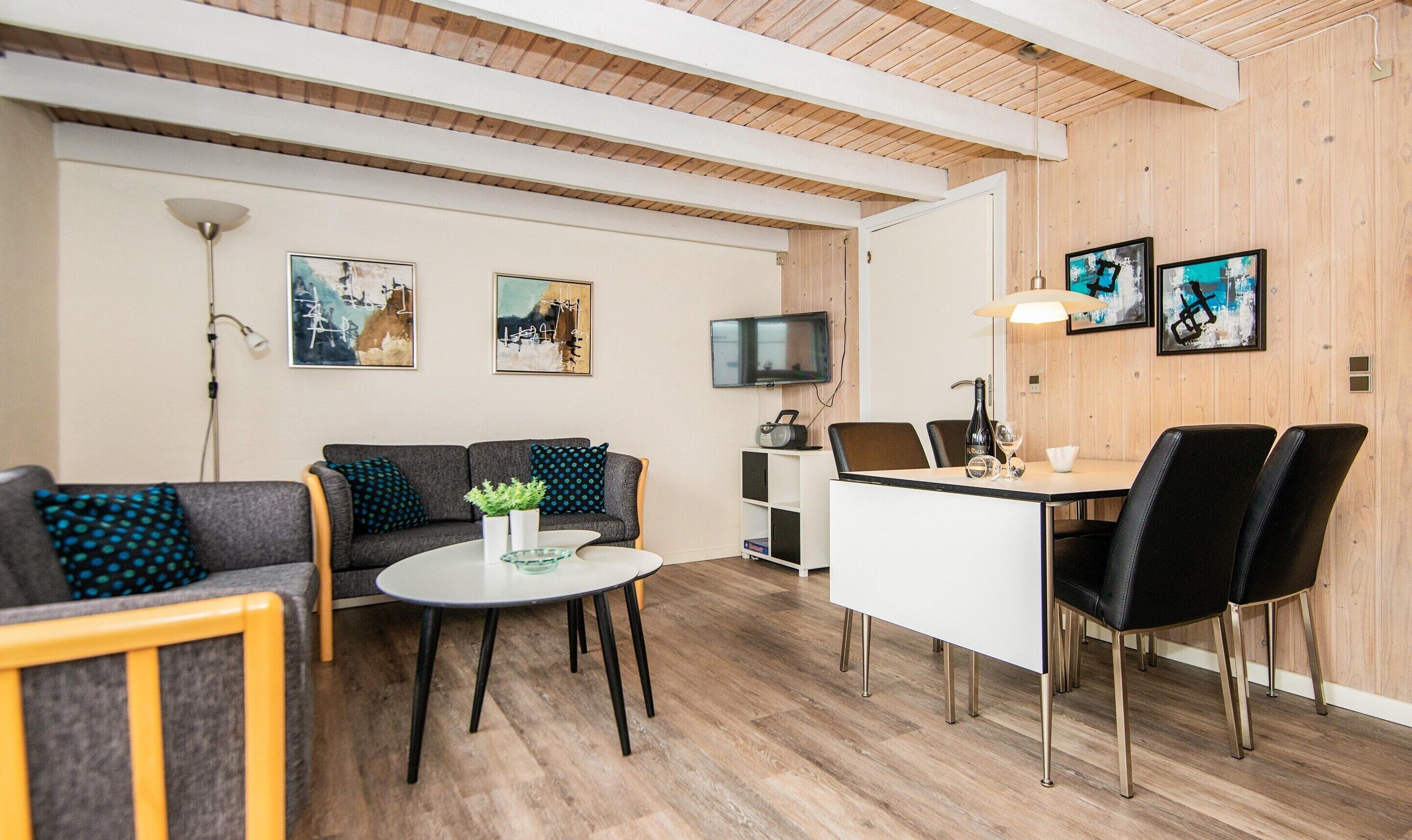 Una sala moderna con un sofá, una mesa de centro redonda, una mesa de comedor con sillas y obras de arte en las paredes.
