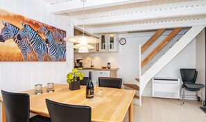 Un comedor con una mesa de madera, sillas, un cuadro de cebras, una cocina con armarios, un reloj y una escalera.
