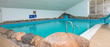 Una piscina interior con borde de piedra, una cascada y un cartel que indica una profundidad de 1,5 metros.