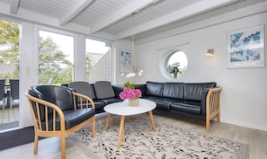 A modern living room with a black leather sofa, a wooden chair, a white coffee table, and a round mirror on the wall. - Bork Harbor: Ringkobing Fjord (Hemmet)