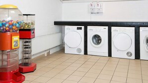Une buanderie équipée de trois machines à laver, d’un distributeur automatique et d’un luminaire au plafond.