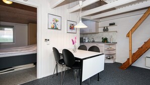 A compact room with a bed, a dining table with chairs, a kitchen area, and a staircase.