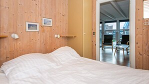 A bedroom with a bed, wooden walls, a door leading to a balcony, and a small table with chairs.