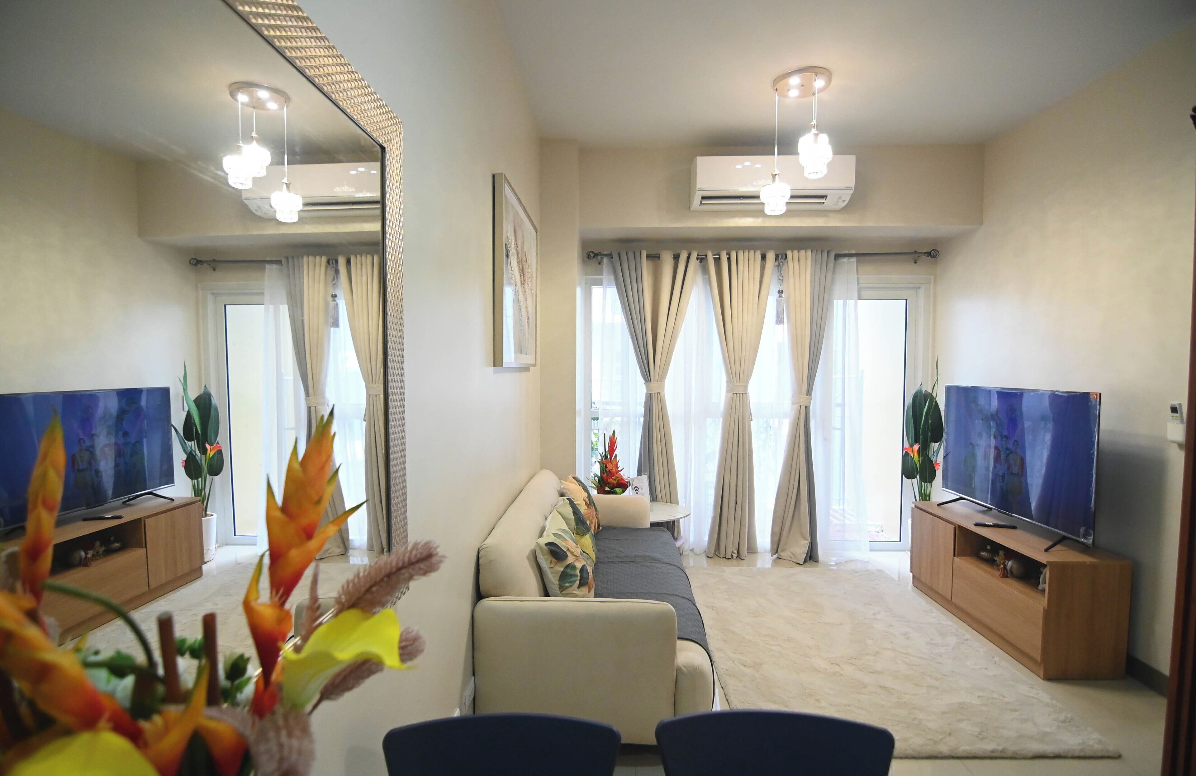 A modern living room with a sofa, two TV screens, a coffee table, and a large mirror.