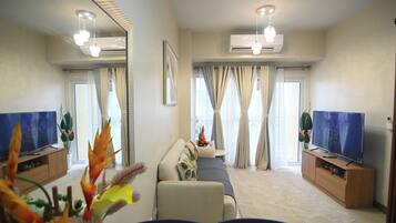 A modern living room with a sofa, two TV screens, a coffee table, and a large mirror.