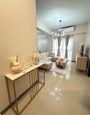A modern living room with a sofa, a coffee table, a console table with decorative items, and a television on a stand. - Kuya Awen's Staycation (Parañaque)