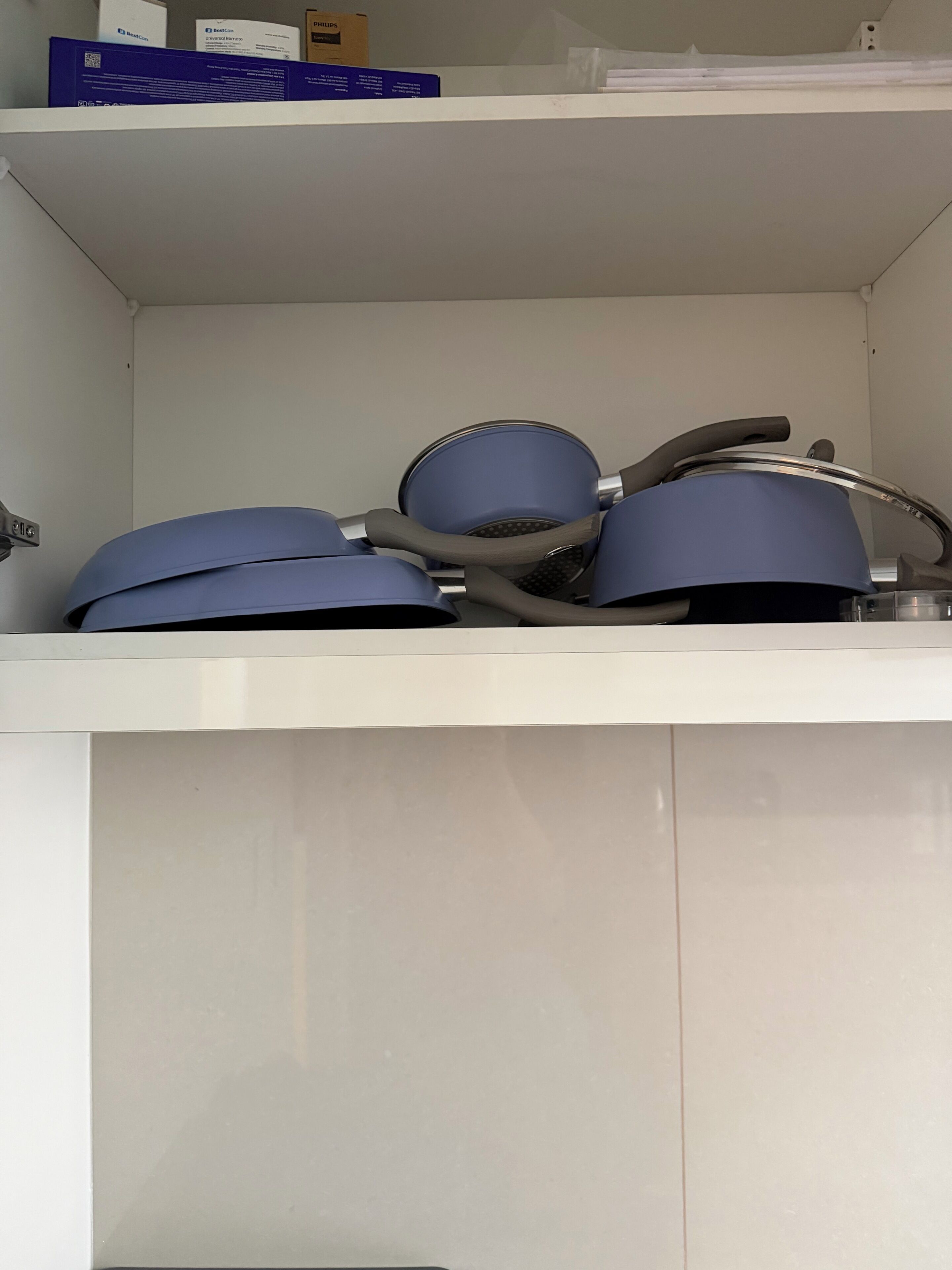 Een keuken met witte kastjes en een plank met dozen erboven.