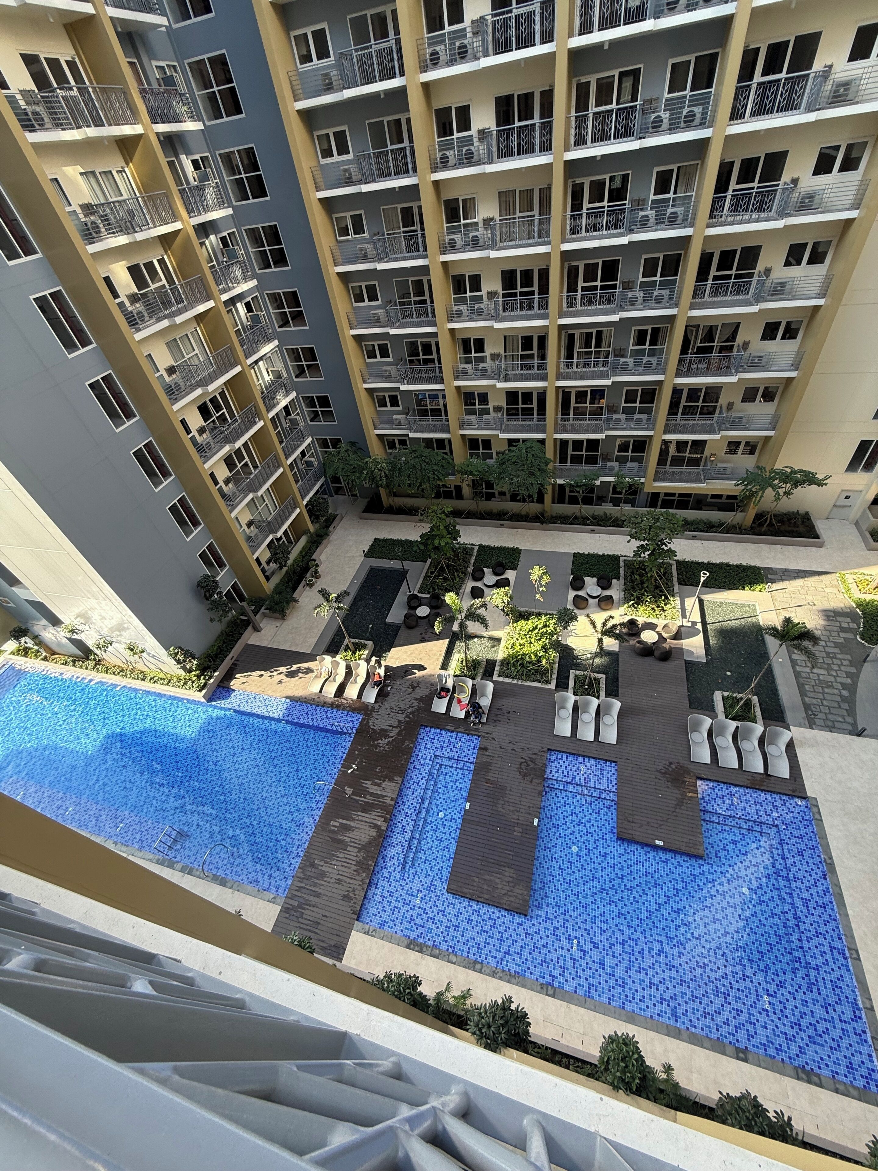 Un edificio residencial de varios pisos con balcones, un área de piscina en la azotea y un patio ajardinado.