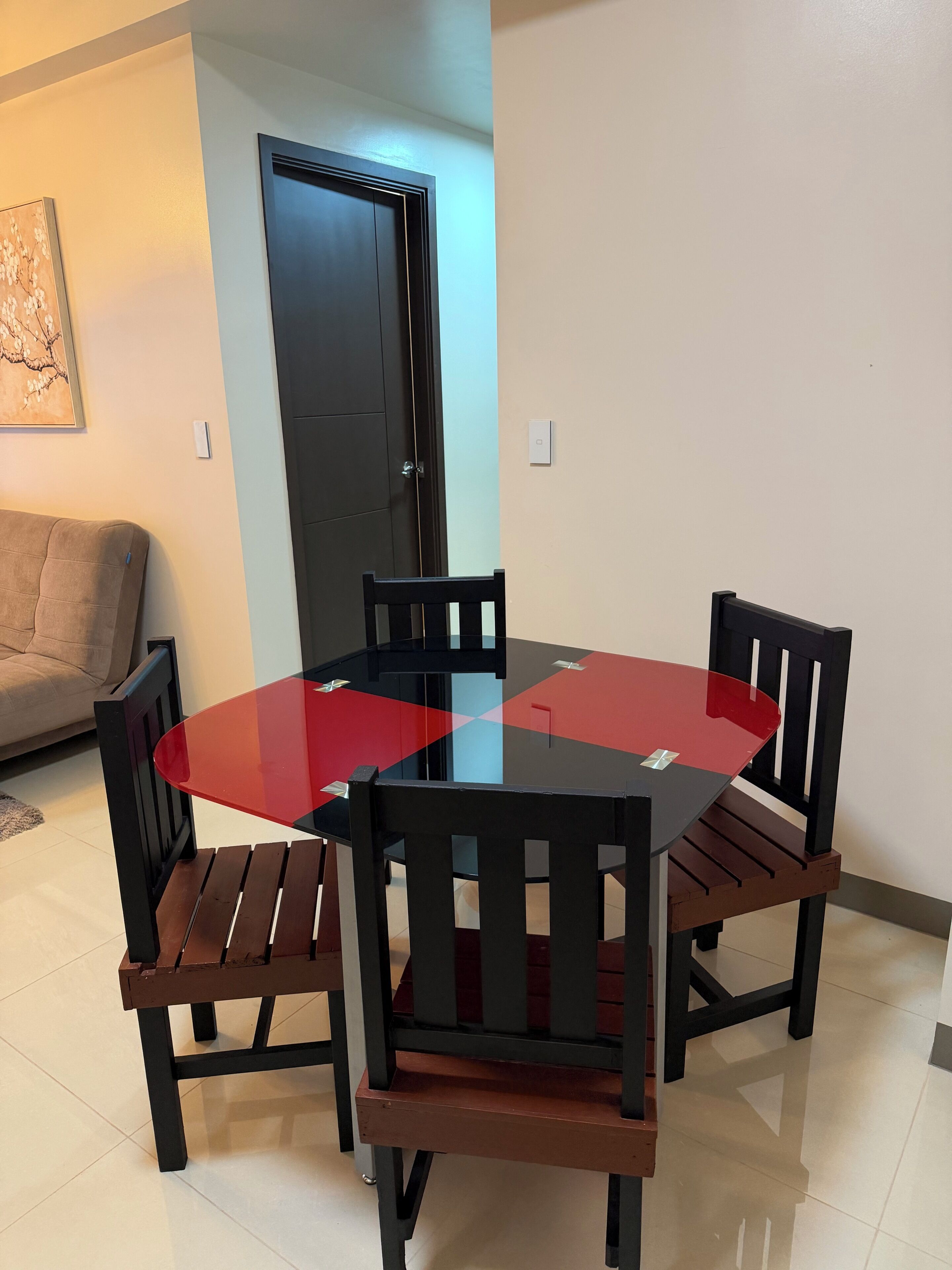A dining area with a round table and four chairs, a door, and a wall-mounted light switch.