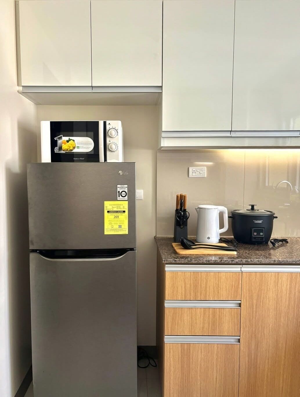 A kitchen with a stainless steel refrigerator, a microwave, a slow cooker, and wooden cabinets.