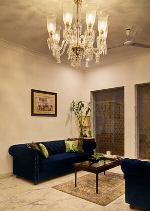 Ein Wohnzimmer mit einer Chandelierleuchte, einem blauen Sofa, einem Couchtisch und einem gerahmten Bild an der Wand.