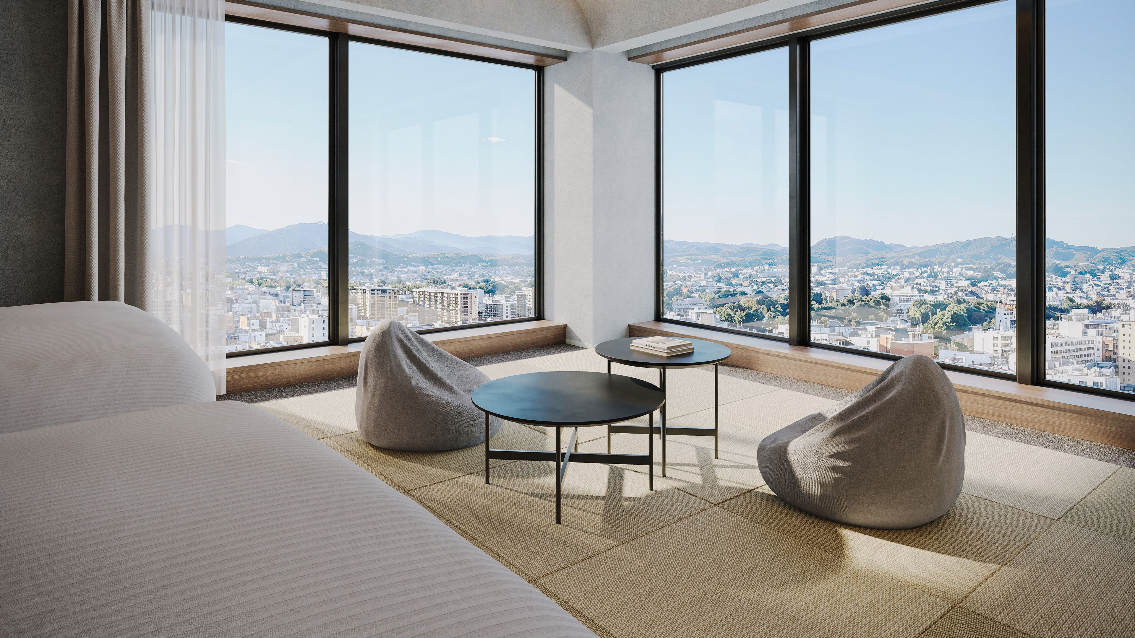 Habitación de hotel con una cama grande, dos sillones de mimbre, una mesita y vistas a un paisaje urbano a través de amplios ventanales.