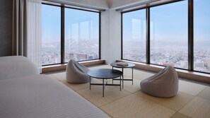 A modern hotel room with a large bed, a small round table, two bean bag chairs, and a view of a cityscape through large windows. - FAV LUX Asahikawa (Asahikawa)