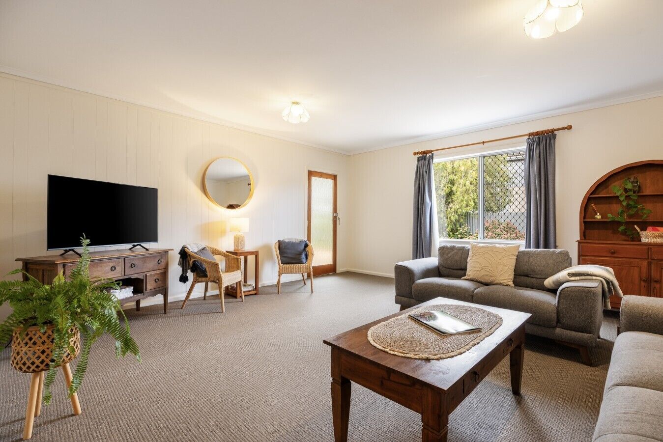 Een woonkamer met een bank, fauteuils, een salontafel, een televisie, een open haard en een groot raam met gordijnen.
