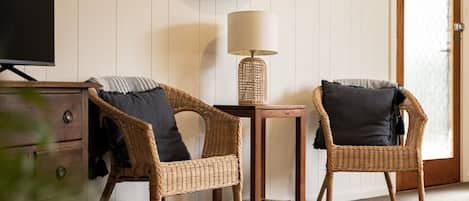A room with two wicker chairs, a small wooden table, a lamp, and a television on a stand.