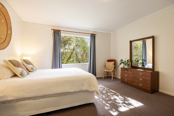 A bedroom with a bed, a dresser, a chair, a window with curtains, and a mirror.
