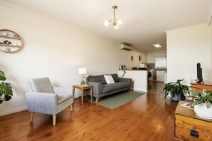 A modern living room with a grey sofa, a small table with a lamp, and a wooden floor.