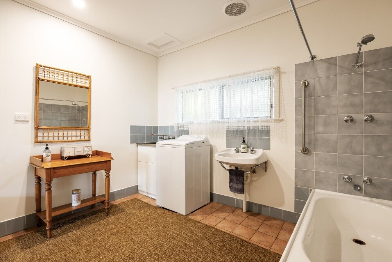 Un bagno compatto con un mobile bagno in legno, una lavatrice, un lavandino finestrato e zona doccia.