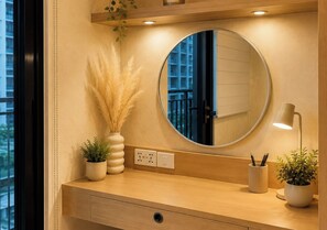 Ein Badezimmer-Waschtisch mit rundem Spiegel, einer kleinen Topfpflanze, einer Lampe und einer wandmontierten Steckdose.