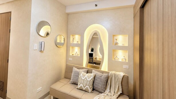 A modern hotel room with a sofa, mirrors, and wall-mounted shelves.