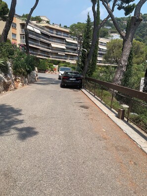 A paved road with a car parked on the side, a stone wall, and a building with multiple balconies in the background. - Elegance, comfort, and a sweeping view (Villefranche-sur-Mer)