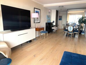 A living room with a flat-screen TV, a piano, a dining table with chairs, and a large window. - Elegance, comfort, and a sweeping view (Villefranche-sur-Mer)
