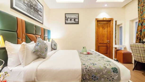 A hotel room with a bed, a desk, a chair, a wooden door, and a framed picture on the wall. - Palette Hotel Cecil Srinagar (Srinagar)