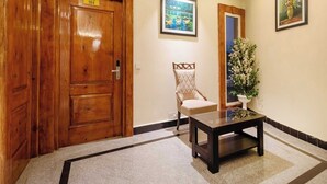 A hotel lobby with a wooden door labeled 'Room No. 104,' a chair, a small table, and two framed pictures on the wall. - Palette Hotel Cecil Srinagar (Srinagar)