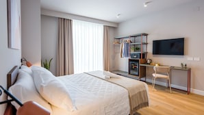 A modern hotel room with a large bed, a desk with a chair, a TV, and a wardrobe.
