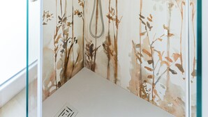 A shower with a floral wall design, a handheld showerhead, and a control panel.