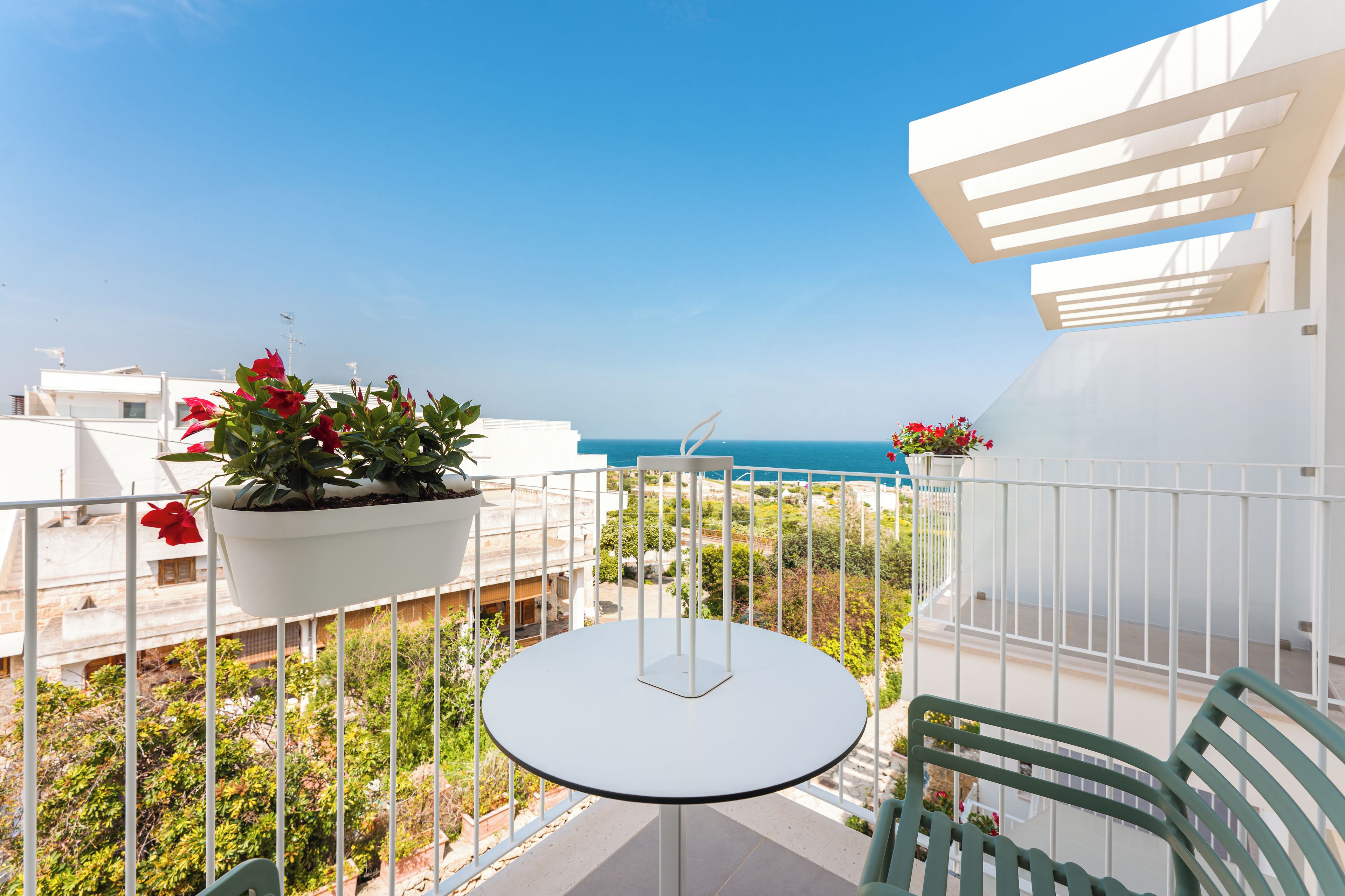 A balcony with a table and chairs, potted plants, and a view of the sea.