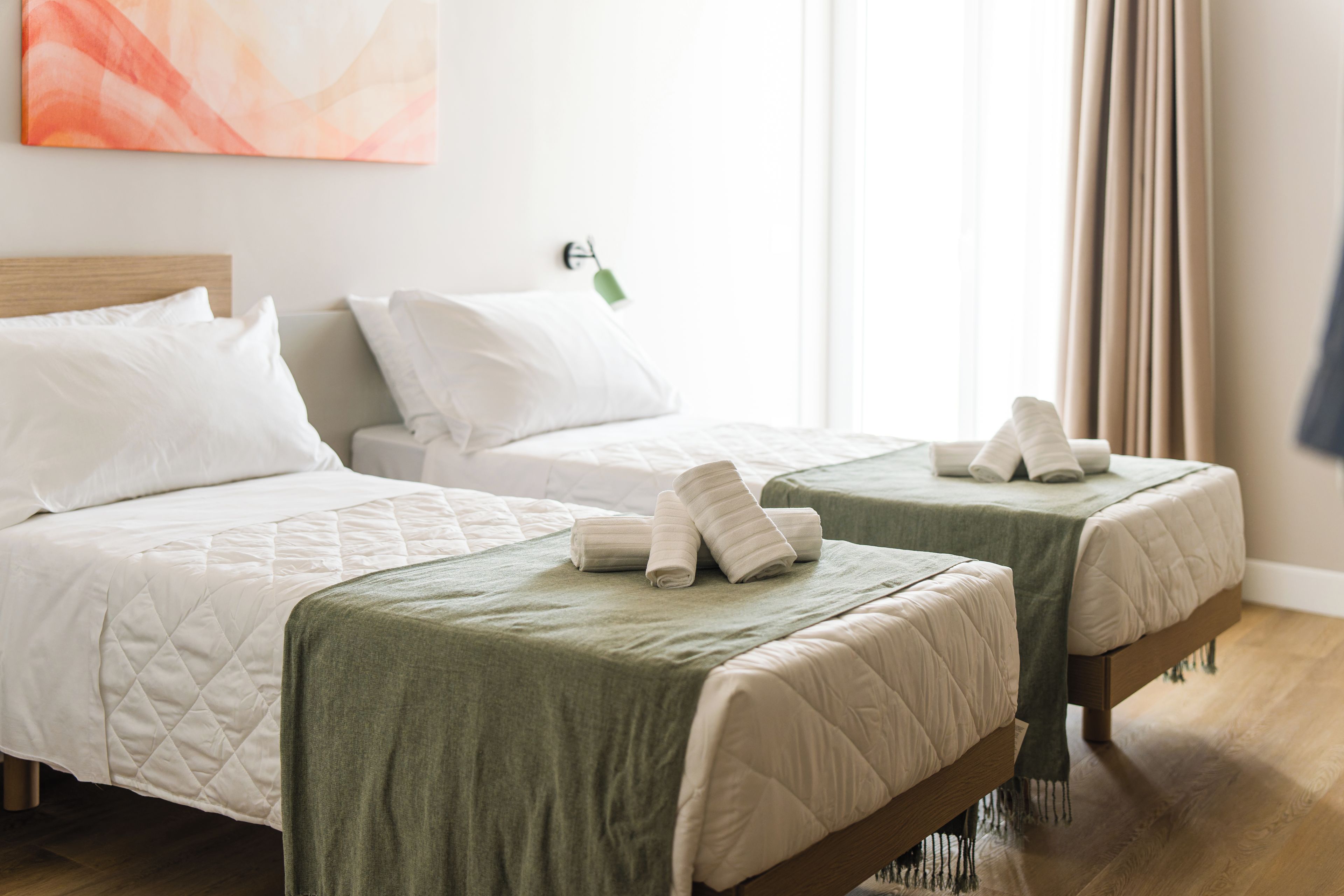 Habitación de hotel con dos camas, una colcha verde, ropa de cama blanca y un cuadro en la pared.