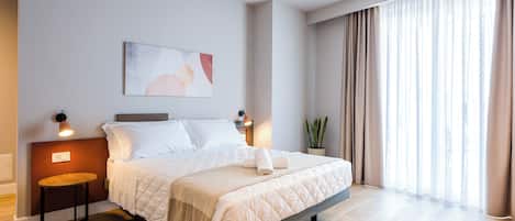 Een moderne hotelkamer met een groot bed, bedlampen, een schilderij, een potplant en uitzicht op het omliggende landschap.