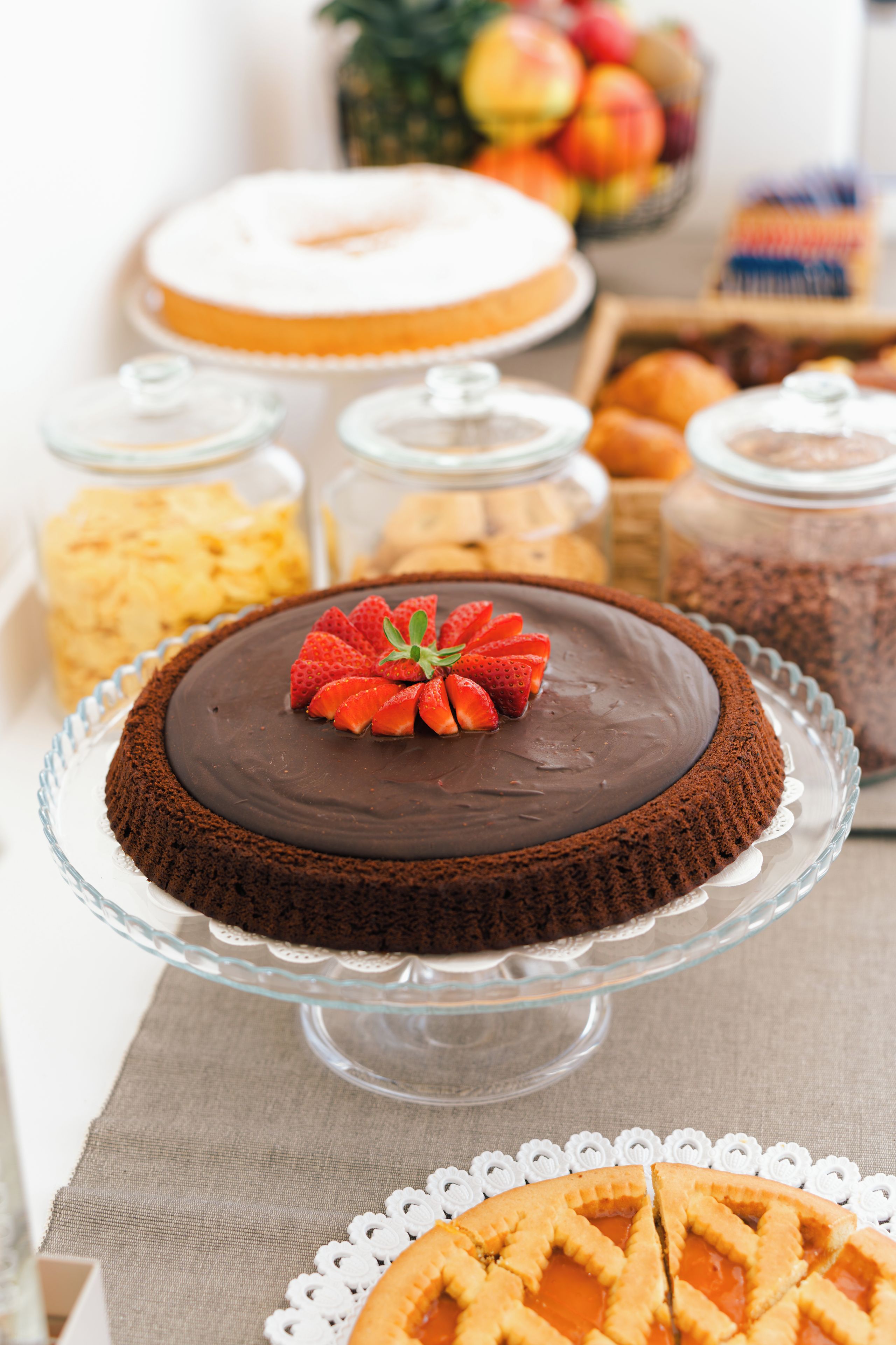 Un tavolo con dolci, una torta al cioccolato guarnita con fragole, circondato da altri dessert e cibi.