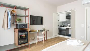 A compact hotel room with a kitchenette, a bed, a desk with a chair, and a TV mounted on the wall.