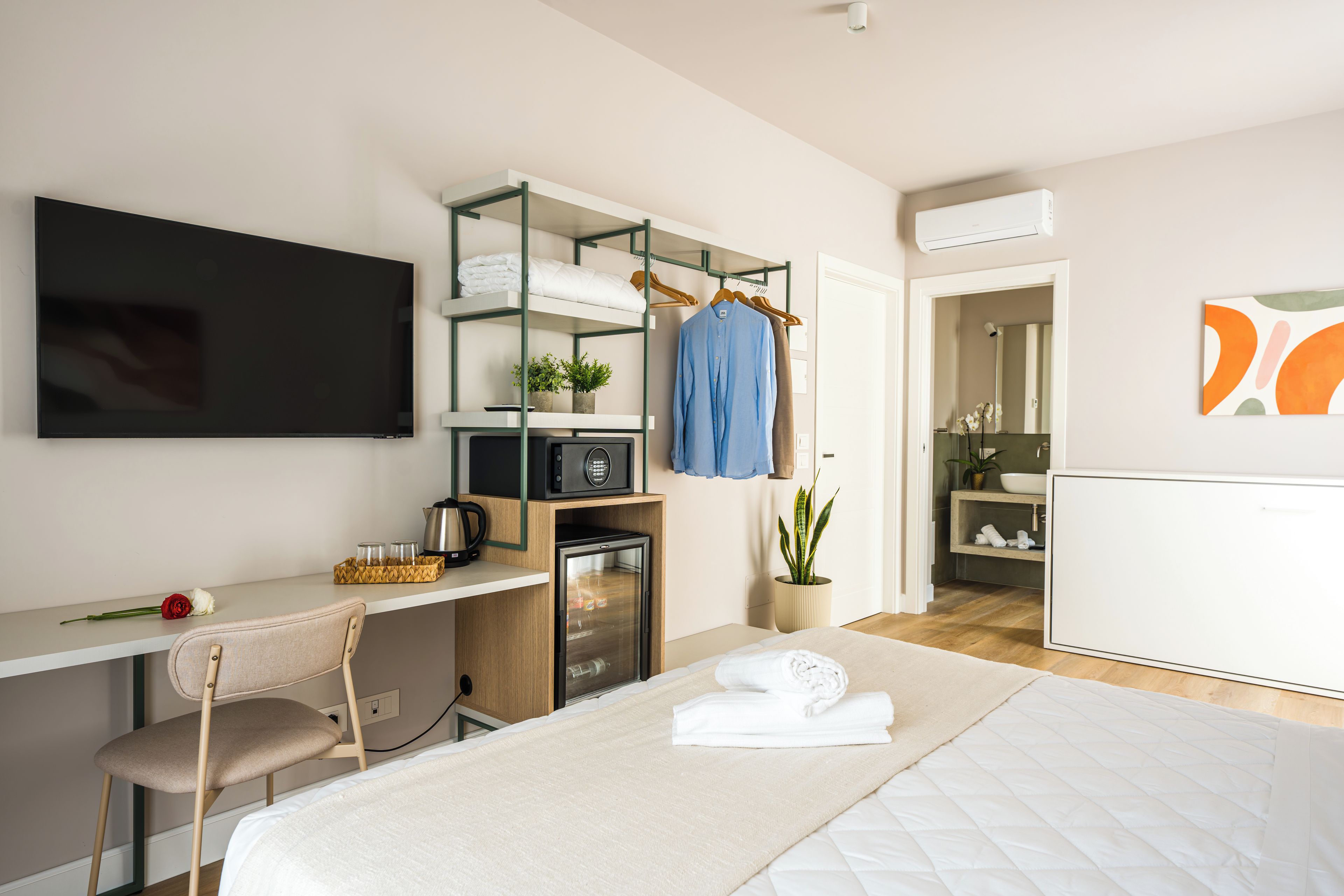 Habitación de hotel moderna con cama, escritorio con computadora, televisor, kitchenette y baño.